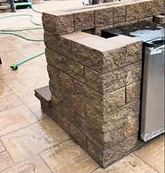 Outdoor kitchen island built in wall block with a built-in fridge, on stamped concrete