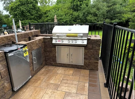 Built-in stainless grill in a stone-faced outdoor kitchen island on a paver deck